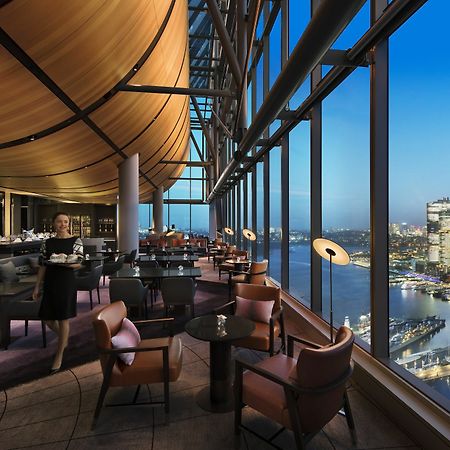 Sofitel Sydney Darling Harbour Hotel Exterior photo The photo shows an elegant restaurant or lounge with a modern, stylish interior. It features large windows that offer a stunning view of a city skyline during twilight or evening. The space is arranged with comfortable seating, including chic chairs 