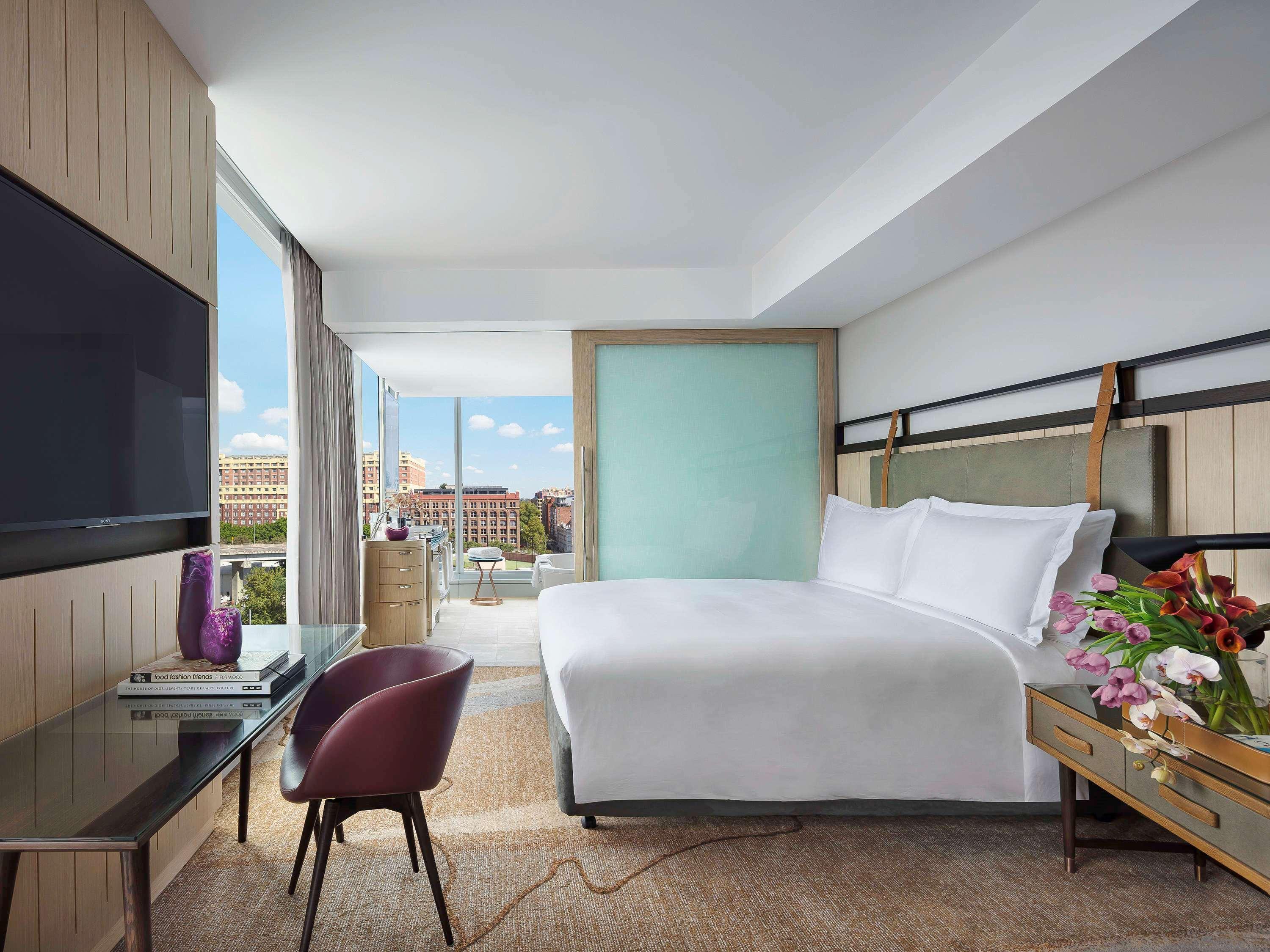 Sofitel Sydney Darling Harbour Hotel Exterior photo The image depicts a modern hotel room featuring a large bed with white bedding, positioned against a contemporary headboard. There is a stylish glass partition separating the sleeping area from another part of the room. A flat-screen television is mo