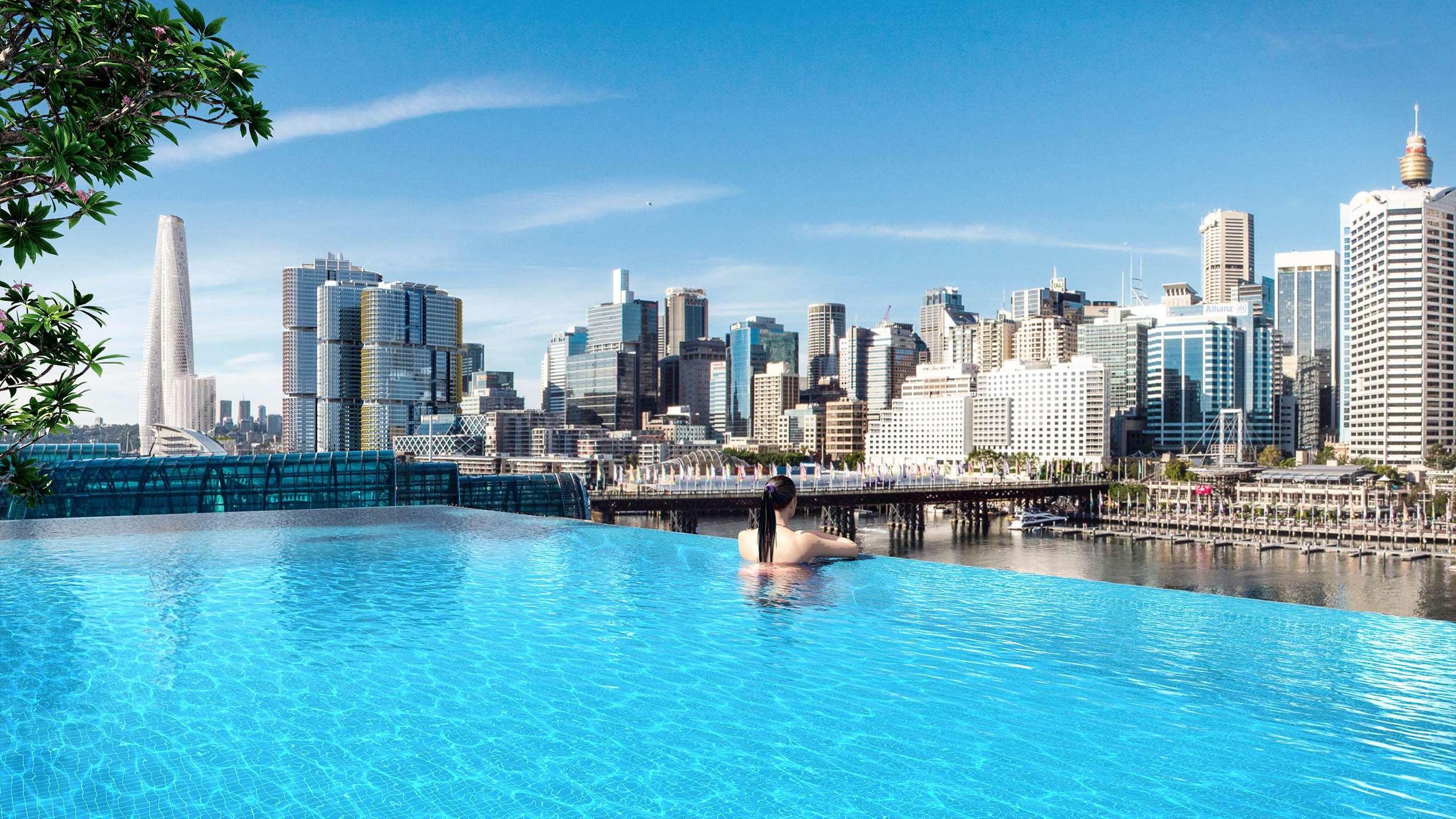 Sofitel Sydney Darling Harbour Hotel Exterior photo The photo shows a stunning urban skyline with a clear blue sky and a modern, luxurious infinity pool in the foreground. The pool appears to extend seamlessly into the horizon, providing a breathtaking view of the cityscape. Skyscrapers of various sty