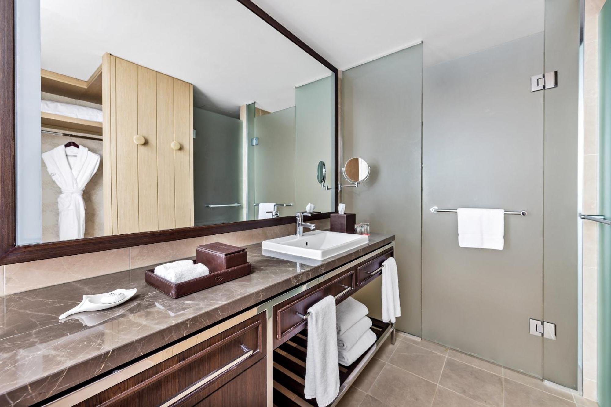 Sofitel Sydney Darling Harbour Hotel Exterior photo The photo shows a modern bathroom with a clean and sleek design. It features a vanity with a dark wooden cabinet and a light-colored countertop. There is a square sink on the counter with a modern faucet. Next to the sink, there are neatly placed toi