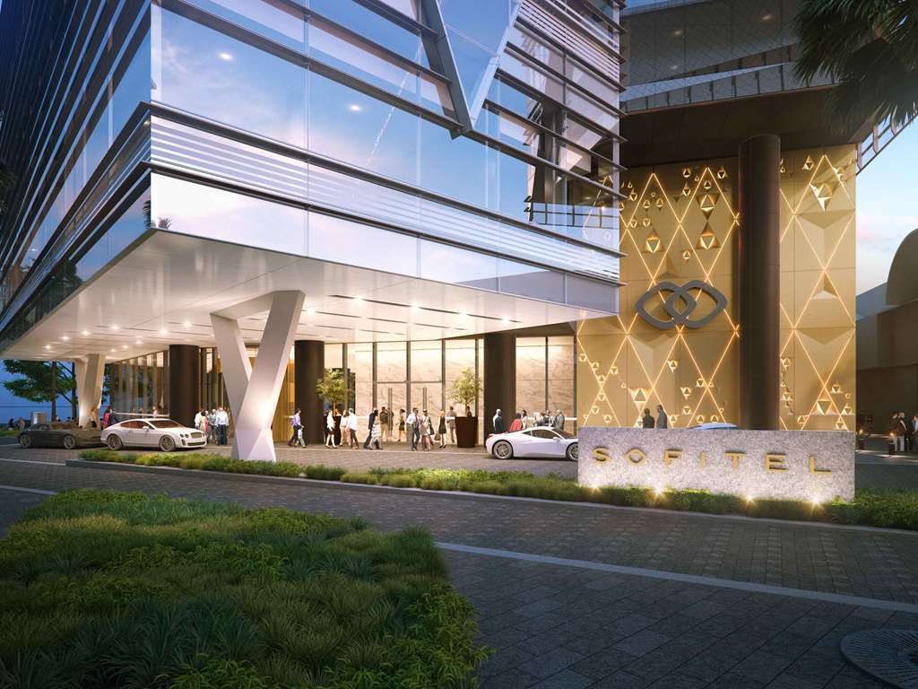 Sofitel Sydney Darling Harbour Hotel Exterior photo The image shows the entrance of a modern hotel, likely the Sofitel brand. The building features a sleek, glass facade with a geometric design that reflects contemporary architecture. In front of the entrance, there is a large stone sign displaying th