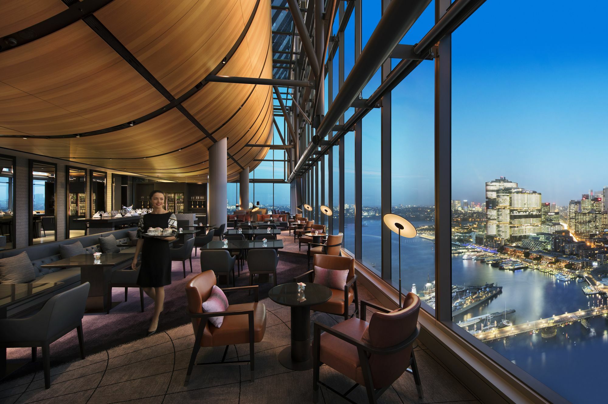 Sofitel Sydney Darling Harbour Hotel Exterior photo The photo shows an elegant restaurant or lounge with a modern, stylish interior. It features large windows that offer a stunning view of a city skyline during twilight or evening. The space is arranged with comfortable seating, including chic chairs 