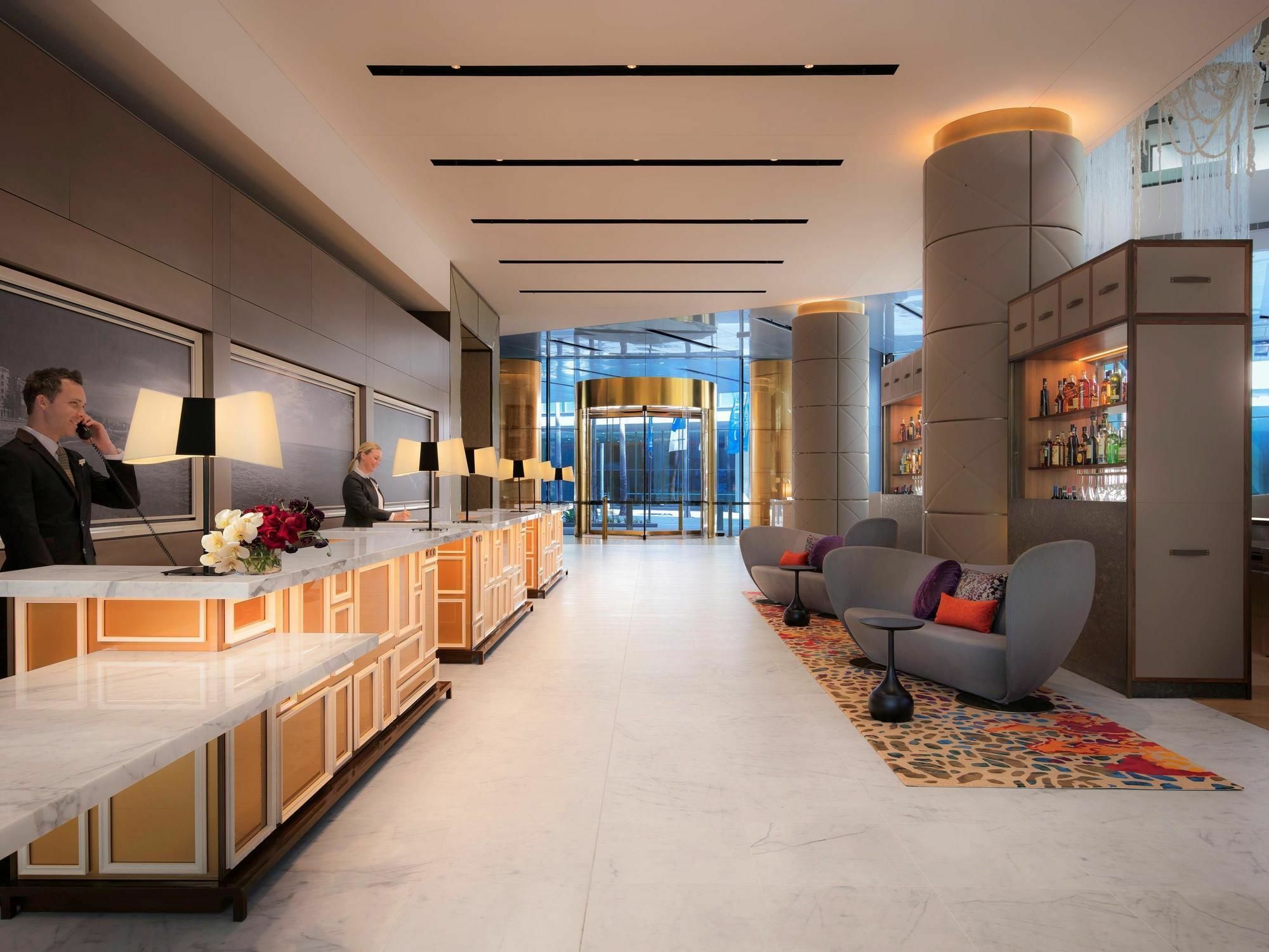 Sofitel Sydney Darling Harbour Hotel Exterior photo The photo shows a modern hotel lobby. It features a spacious area with a sleek and contemporary design. On the left side, there is a reception desk with several staff members attending to guests. The desk is illuminated with warm lighting and is deco
