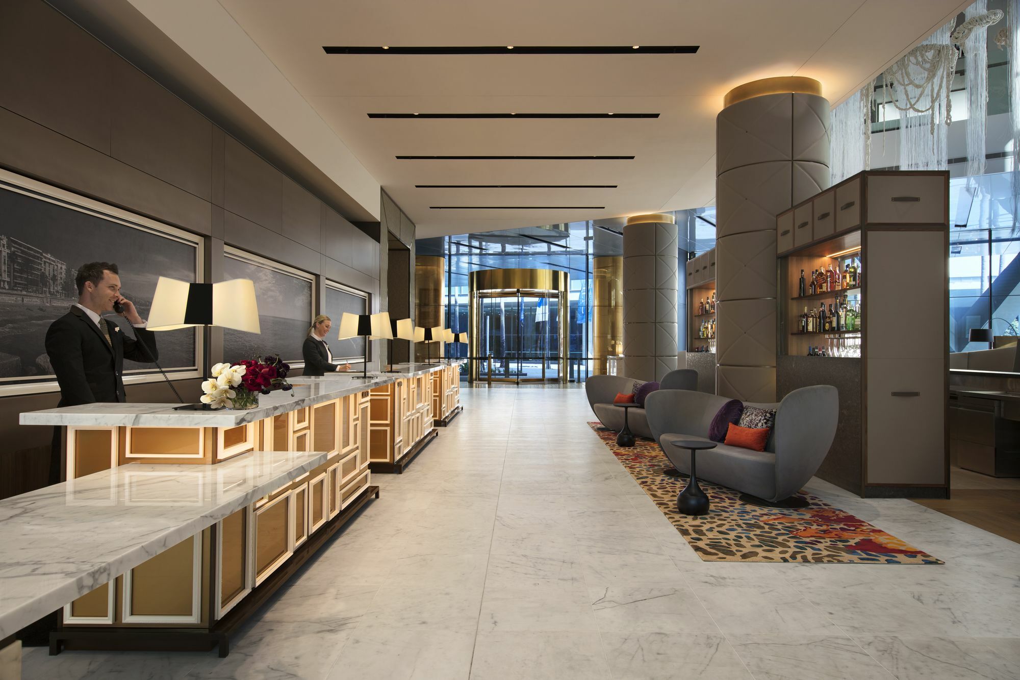 Sofitel Sydney Darling Harbour Hotel Exterior photo The photo shows the interior of a modern hotel lobby. There are two reception desks with staff members attending to guests. The lobby features elegant decor, including stylish lighting and a combination of warm and neutral colors. To the side, there 
