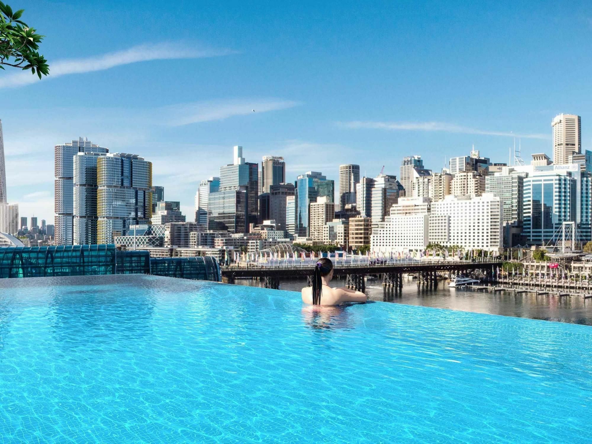 Sofitel Sydney Darling Harbour Hotel Exterior photo The image shows a stunning infinity pool with crystal-clear water, creating a seamless view towards a city skyline in the background. The skyline features modern skyscrapers with reflective glass facades. The scene conveys a tranquil and luxurious at