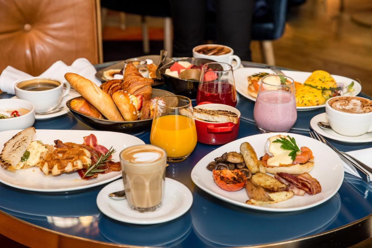 Sofitel Sydney Darling Harbour Hotel Exterior photo The photo showcases a lavish breakfast spread on a table. There are various items, including:

- Several baked goods such as croissants and breadsticks.
- A plate with a serving of eggs, likely scrambled or poached, along with bacon and sausage.
- A 