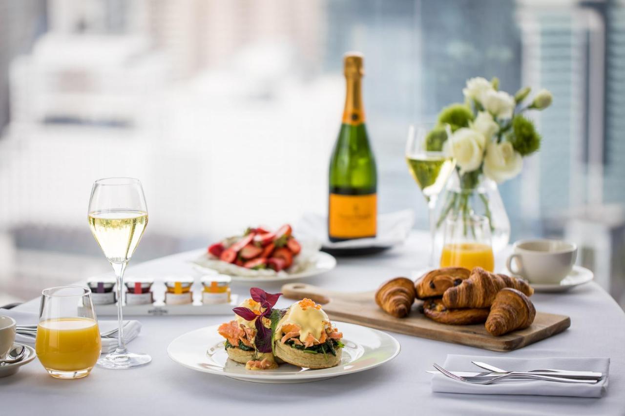 Sofitel Sydney Darling Harbour Hotel Exterior photo The photo displays a beautifully arranged breakfast or brunch setting. There is a plate featuring a gourmet dish, possibly eggs with colorful garnishes, alongside two golden-brown croissants. A glass of sparkling wine is prominently placed, alongside